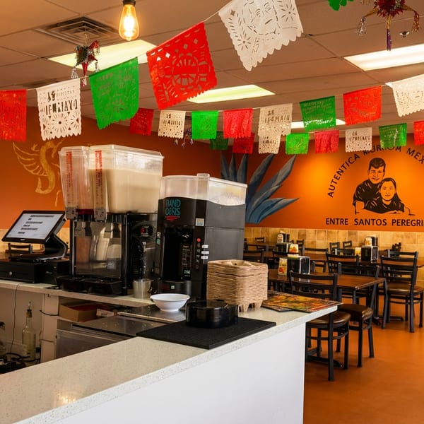 Vibrant Mexican restaurant interior with colorful papel picado, wall murals, a service counter, and dining tables.